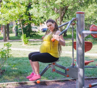 Pregnant Woman is exercising outdoors in public fitness machines.