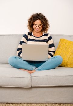 Beautiful woman at home sitting on the sofa working with a laptop