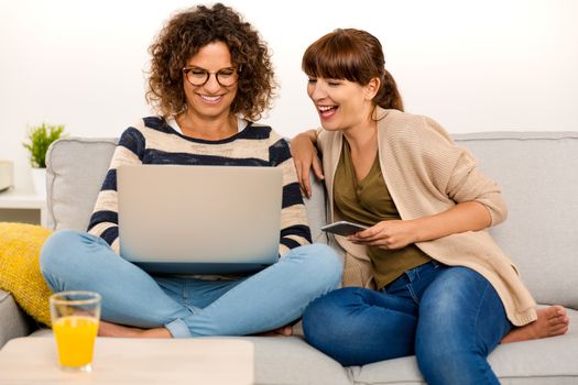 Two beautiful women at home working with a laptop