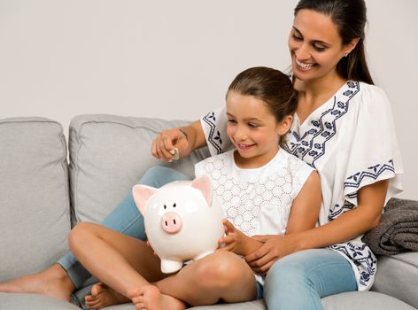 Mother and daughter putting coins into a piggy bank