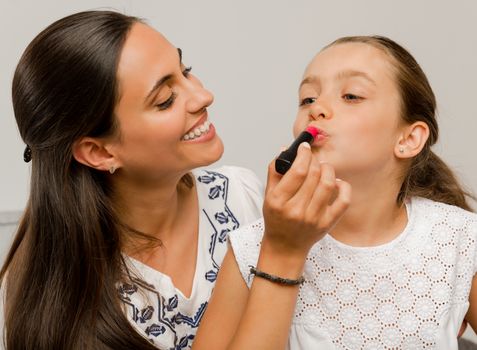 Mother playing with her daughter applying lipstick