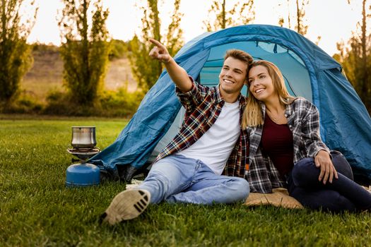 Shot of a happy couple camping on the nature and pointing to somewhere