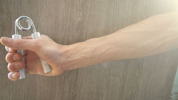 young athlete compresses and decompresses silver metallic manual expander.