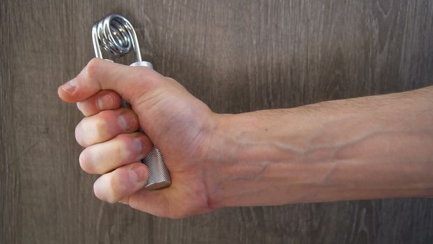young athlete compresses and decompresses silver metallic manual expander.
