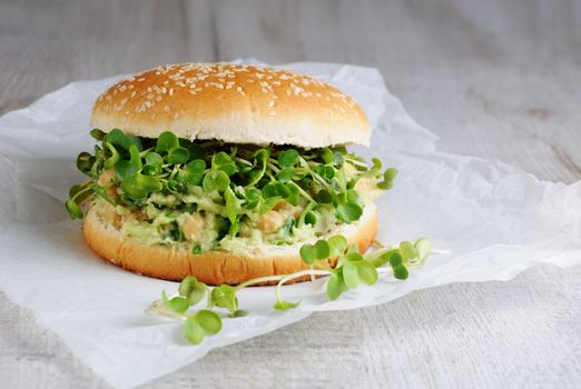 A vegetarian burger made from a gluten-free bun with chickpeas, avocado and herbs, radish sprouts. A quick and healthy lunch idea that you feel energized throughout the day.