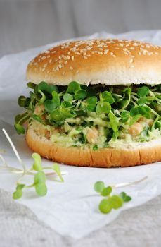 A vegetarian burger made from a gluten-free bun with chickpeas, avocado and herbs, radish sprouts. A quick and healthy lunch idea that you feel energized throughout the day.