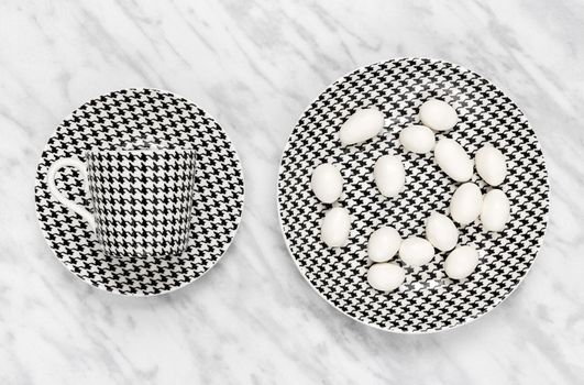Black and white coffee cup and white chocolate on a plate, on marble background.