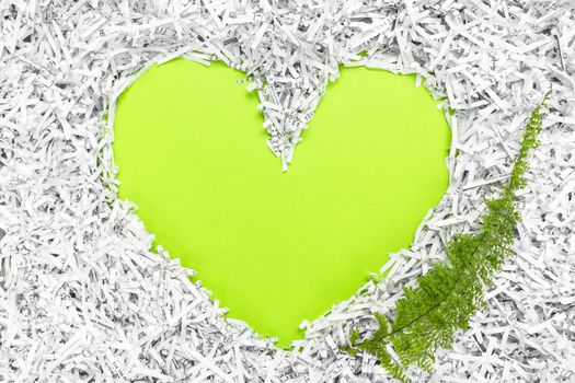 Heart frame made of shredded paper and a green leaf. Recycling and environment conservation concept.