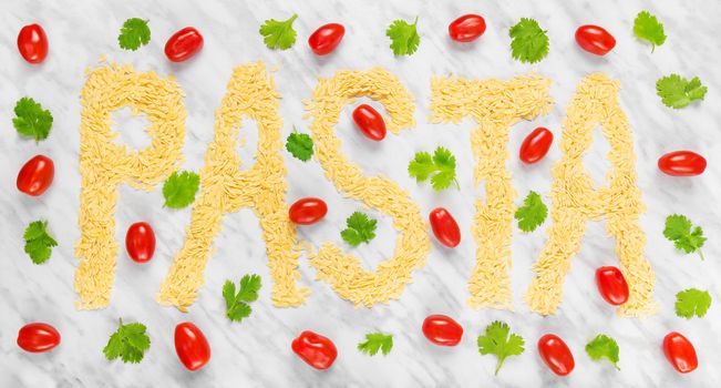 The word "PASTA" written with rice-shaped tiny Orzo pasta on marble background, decorated with tomatoes and coriander.