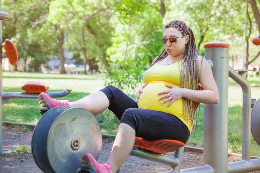 Pregnant woman on a cycling exercise machine in the park.