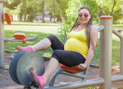 Smiling pregnant woman on a cycling exercise machine in the park.