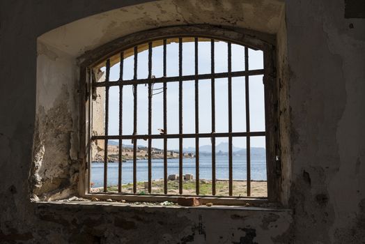 view from inside prison cell to the beautifull nature of the maddalena archipel in italy with blue sea and plants and flowers