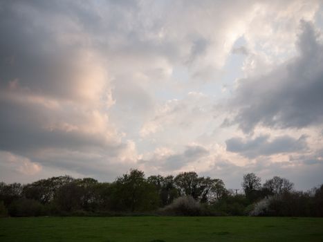 Sun setting over field with trees dramatic clouds nature background; essex; england; uk