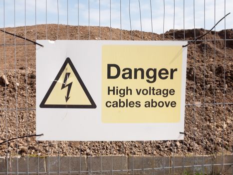 close up construction site fence sign: danger high voltage cables above; essex; england; uk