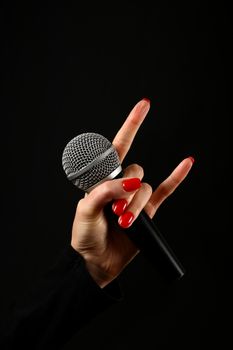 Woman hand with red nails holding microphone with devil horns rock metal sign isolated on black background