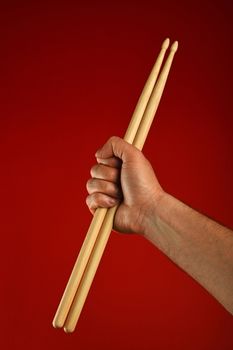 Man hand holding two wooden drumsticks over red background, diagonal, close up