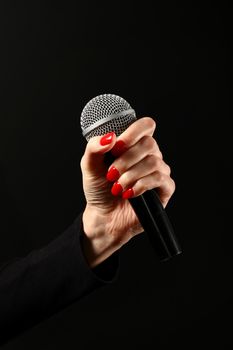 Woman hand with red nails holding microphone isolated on black background