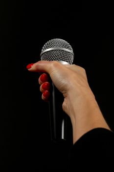 Woman hand with red nails holding microphone isolated on black background