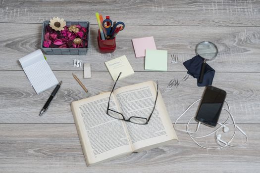 A book, cellphone, reminder and glasses on an old wooden desk