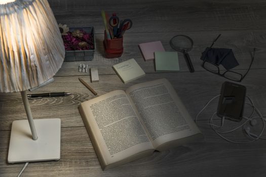 A book, cellphone, reminder and glasses on an old wooden desk