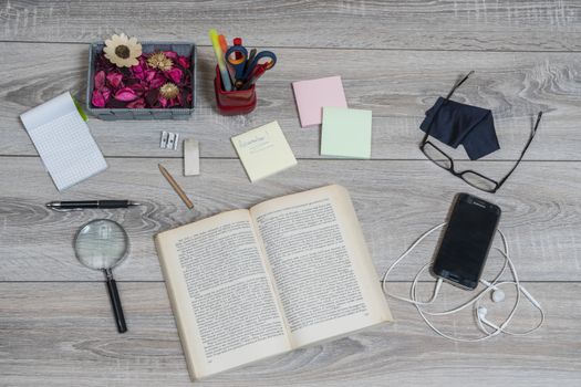 A book, cellphone, reminder and glasses on an old wooden desk