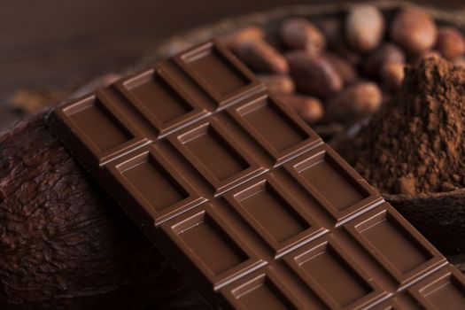 Chocolate bar, candy sweet, cacao beans and powder on wooden background