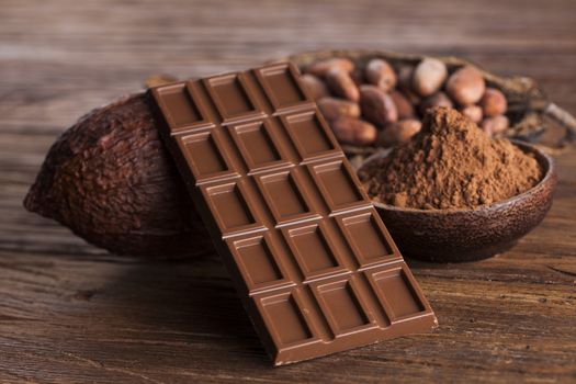 Chocolate bar, candy sweet, cacao beans and powder on wooden background