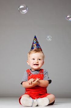 happy baby boy with birthday hat and foam balloons, studio shot