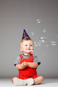 happy baby boy with birthday hat and foam balloons, studio shot