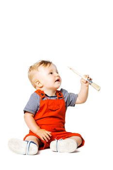 baby boy sitting on the floor, holding paint brush, isolated on white