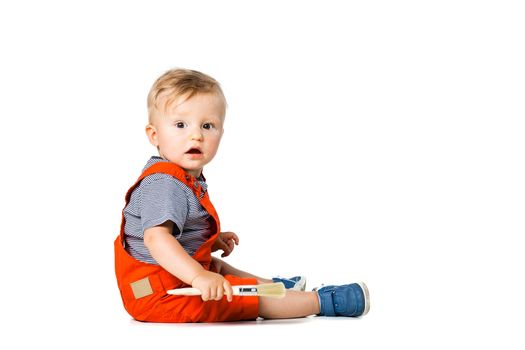 baby boy sitting on the floor, holding paint brush, isolated on white