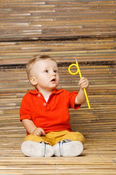 baby boy sitting on the floor, holding a pencil, on bamboo background