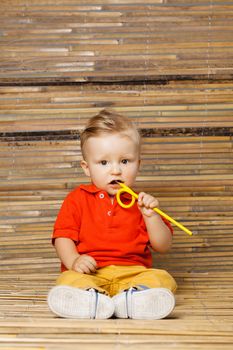 baby boy sitting on the floor, holding a pencil, on bamboo background