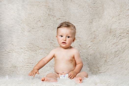 baby boy in diapers, sitting on a shaggy woolen homemade blanket