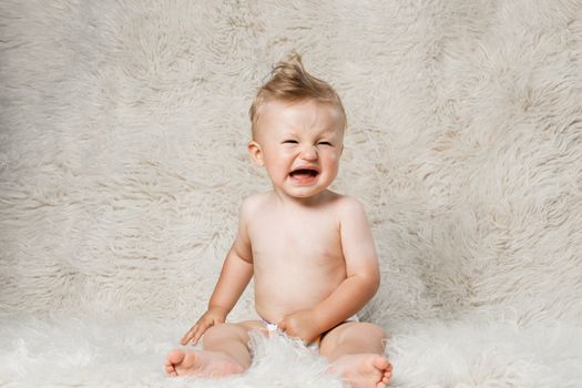 crying baby boy in diapers, sitting on a shaggy woolen homemade blanket