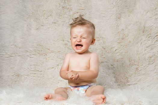 crying baby boy in diapers, sitting on a shaggy woolen homemade blanket