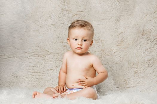 baby boy in diapers, sitting on a shaggy woolen homemade blanket