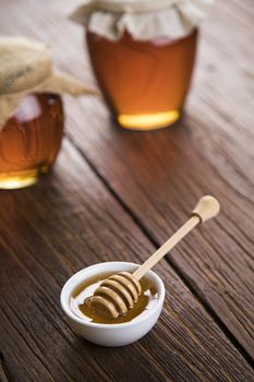 Honey dripping from a wooden honey dipper in a jar on wooden background