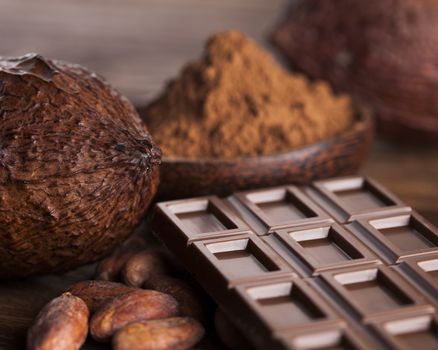 Chocolate bar, candy sweet, cacao beans and powder on wooden background