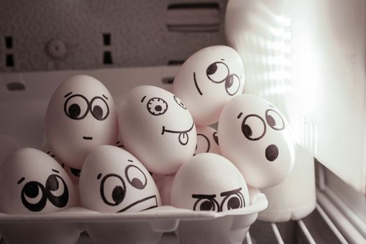 Concept of evening with friends on sofa. Face eggs are funny in the fridge. Photo for your design. A group of eggs is warmed by the light.
