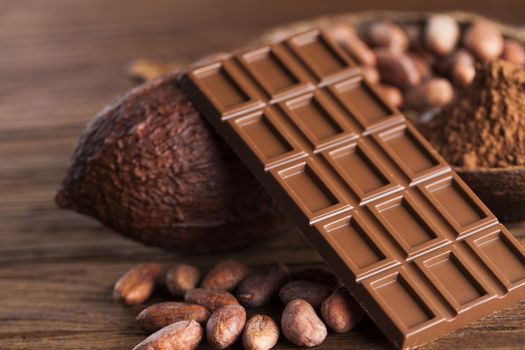 Chocolate bar, candy sweet, cacao beans and powder on wooden background