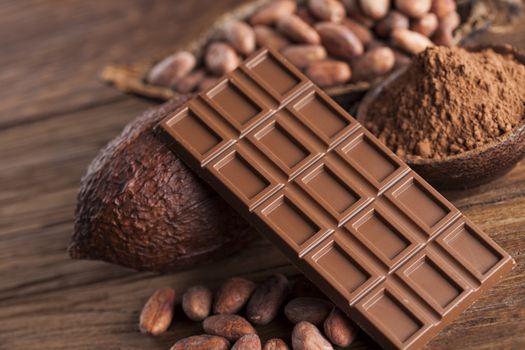 Chocolate bar, candy sweet, cacao beans and powder on wooden background