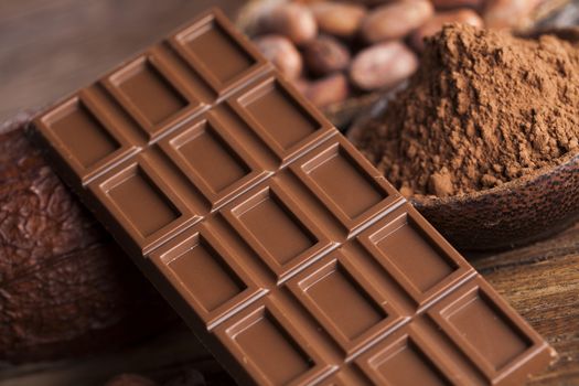 Chocolate bar, candy sweet, cacao beans and powder on wooden background