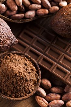 Chocolate bar, candy sweet, cacao beans and powder on wooden background