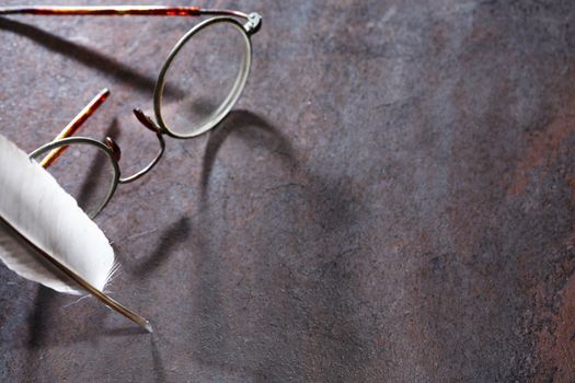 Closeup of old spectacles near feather on dark background with shadow