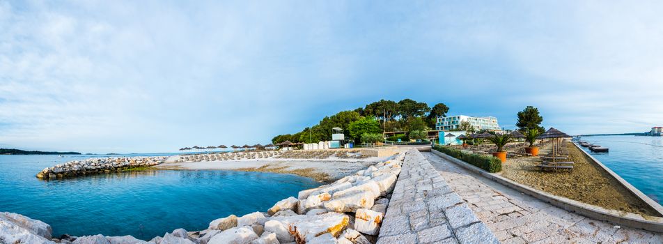 Beach and resort with beach chairs in morning light on the beach of a Croatian seaside holiday resort in Porec, Istria, no people