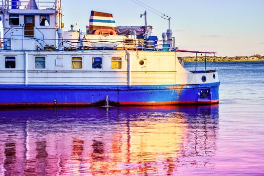 A cruise tourist ship is reflected in the water at dawn.