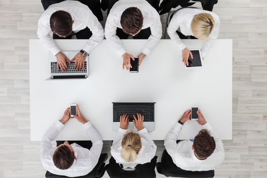 Business people working with digital devices sitting around white table