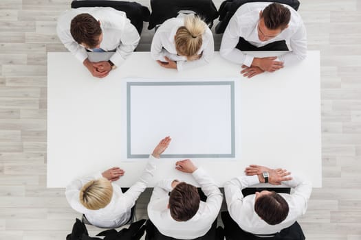 Business people sitting around empty table, business man pointing to blank copy space in the middle