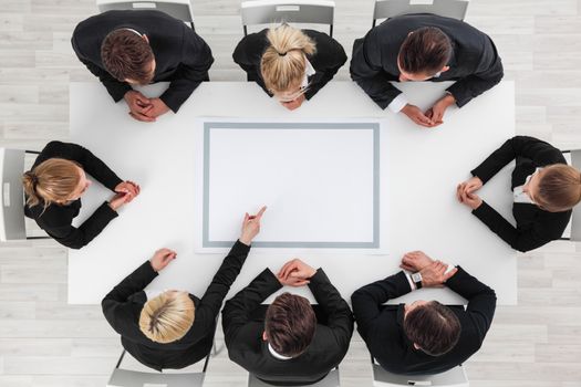 Business people sitting around empty table, business man pointing to blank copy space in the middle